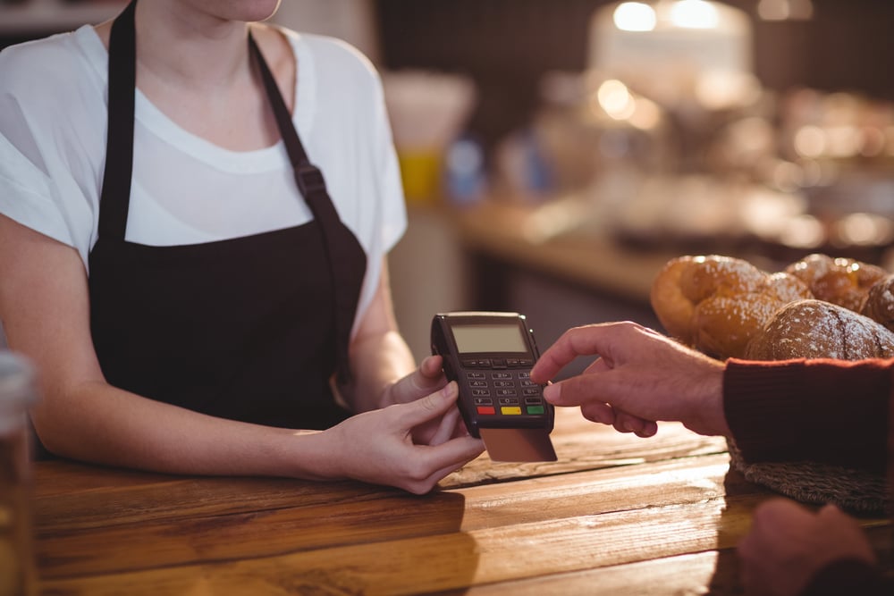 Customer entering pin number into machine at counter in cafe